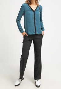 Tealblus med svart kant och V-ringning, i kombination med svarta skräddarsydda byxor och vita skor med svarta accenter. Anmärkningsvärda skräddarsydda detaljer.