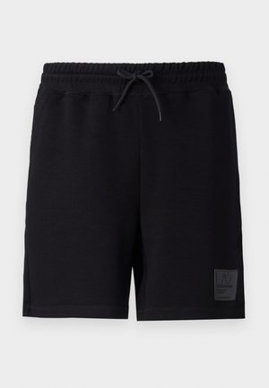 Housut mustasta puuvillasta, joissa on joustava vyötärö ja nyöri. Vasemmassa jalassa on teksturoitu ommelbrändäys.