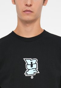 Black cotton t-shirt featuring a multi-layered cyan and white logo design on the left side. Ribbed neckline with a smooth texture.