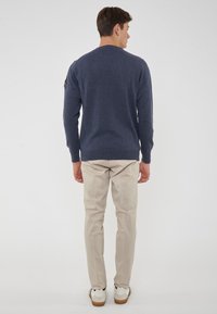 Maglione lavorato a maglia blu navy con maniche lunghe, scollo rotondo e orlo a costine. Abbinato a pantaloni beige e sneaker bianche.