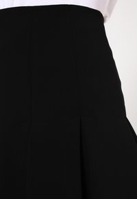 Musta laskostettu hame, jossa on rakenteellinen vyötärö ja sileä pinta. Ominaisuuksiin kuuluu tarkka ompelu ja siisti, minimalistinen muotoilu.