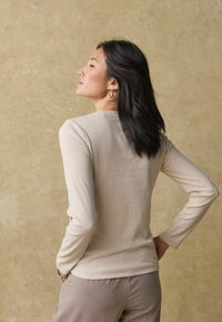 Top beige chiaro a maniche lunghe realizzato in tessuto a costine, con scollatura rotonda e design aderente, abbinato a pantaloni beige coordinati.