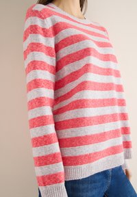 Rot- und grau gestreifter Pullover mit weicher Textur, ausgestattet mit Rundhalsausschnitt und geripptem Saum, kombiniert mit blauen Jeans aus Denim.