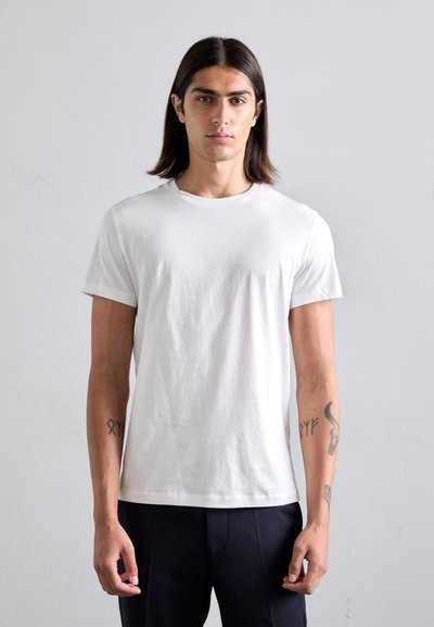 Slim-fit, korte mouwen witte katoenen t-shirt met een ronde hals. Egaal textuur, minimalistisch design, gedragen met marineblauwe broek.
