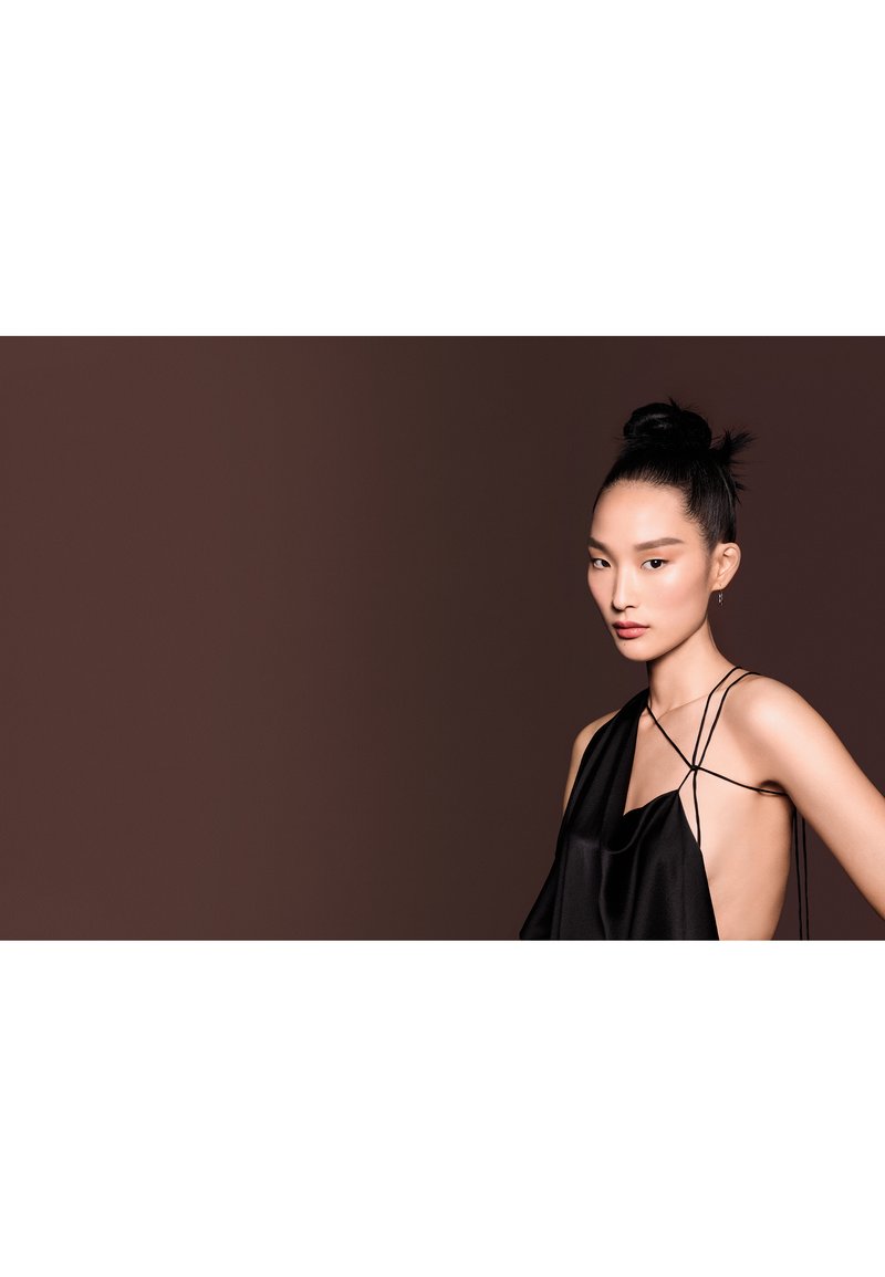 Haut en satin noir avec une coupe ample, doté de fines bretelles, d'un design asymétrique et d'un décolleté plongeant sur un fond marron.