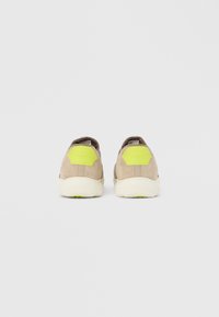 Baskets en daim beige avec une semelle blanche. Dotées d'un accent hexagonal vert vif au talon et d'une texture lisse.
