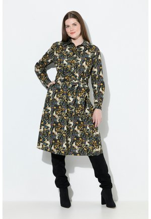Langärmliges Hemdkleid aus dunklem Stoff mit buntem Blumen- und Tierdruck, tailliertem Schnitt und knielangem Saum. Schwarze, hochhackige Stiefel.