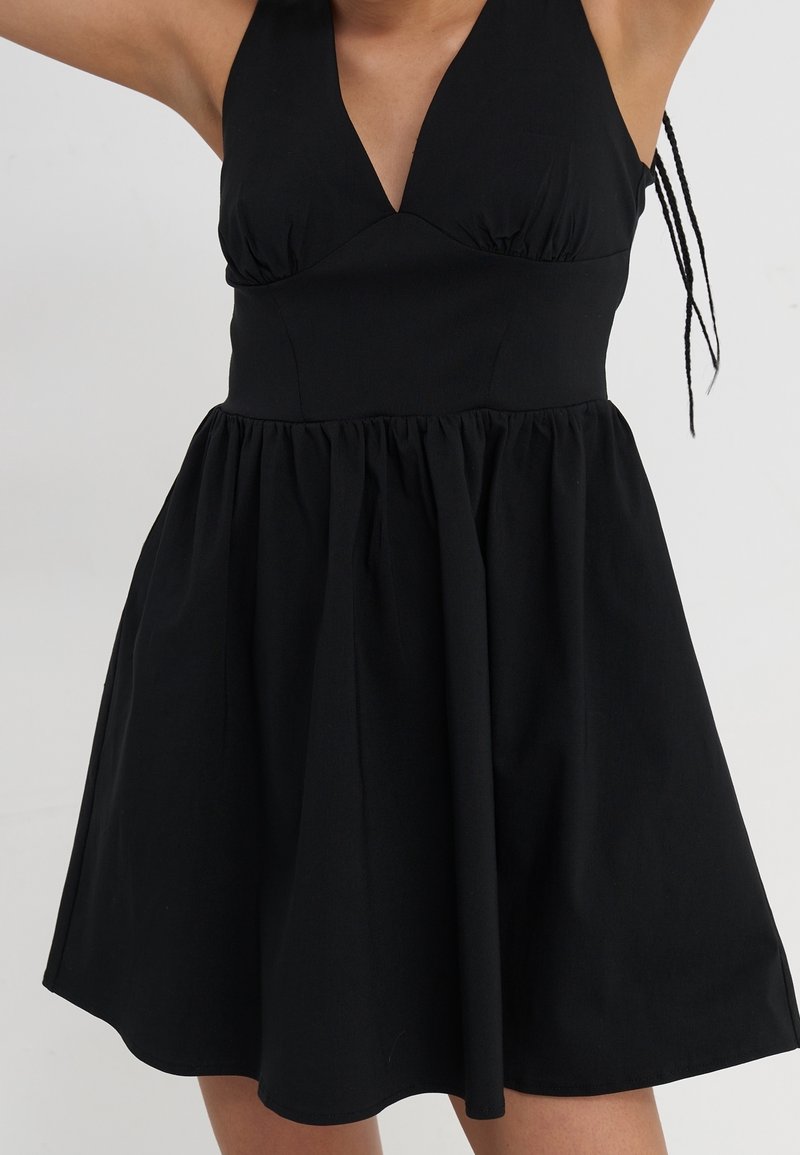 Robe noire sans manches avec un décolleté en V profond, un corsage ajusté et une jupe évasée. Confectionnée en tissu léger à texture lisse.