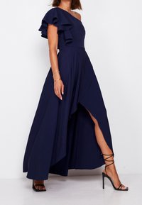 Mörkblå, enaxlad klänning med volangdetaljer, plisserad design, hög slits och kombinerad med svarta, strappy högklackade sandaler.