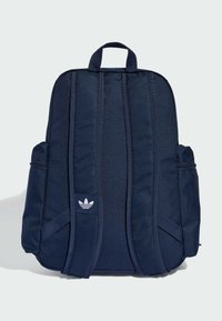 Granatowy plecak wykonany z materiału, wyposażony w dwie boczne kieszenie, uchwyt na górze oraz biały logo z przodu, z wyściełanymi szelkami.