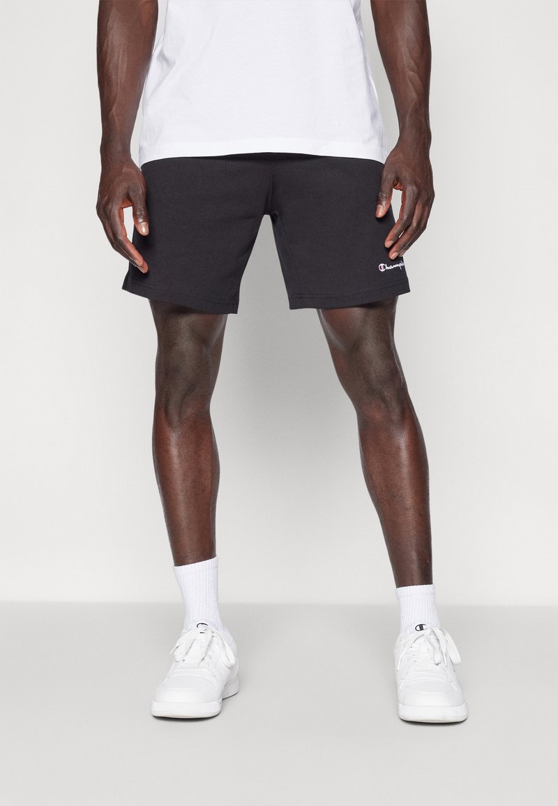 Black cotton shorts with a classic fit, featuring a white embroidered logo on the left leg, paired with white sneakers and ribbed socks.