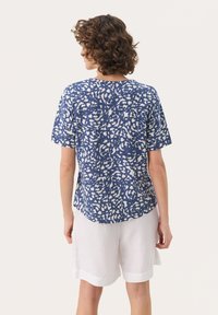 Kortärmad, blåmönstrad skjorta med en vit abstrakt design, tillverkad av lätt material, har en avslappnad passform och rundad nederkant.