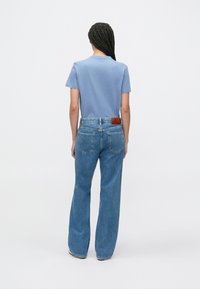 Tricou din bumbac albastru deschis asortat cu blugi din denim albastru cu talie înaltă și croială largă pe picior. Cusături vizibile, două buzunare în spate și un patch din piele cu branding.