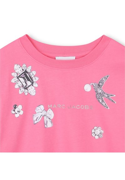 Rosa t-shirt med glänsande detaljer: blommor, rosetter och en fågeldesign, med "MARC JACOBS" i silvertext över framsidan.