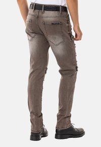 Braune Jeans mit schmaler Passform, ausgeblichener Textur, mehreren Taschen und einem schwarzen Gürtel. Standardnähte und Hardware-Details.