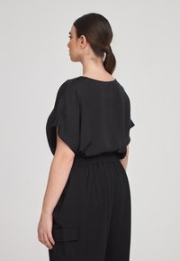 Tuta nera con maniche corte, vestibilità rilassata, elastico in vita e tasche laterali. Tessuto morbido con un design semplice.