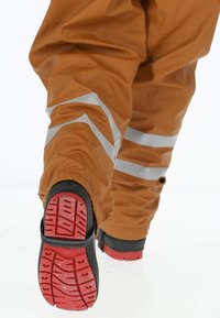 Oranje waterdichte overalls met reflecterende strepen. De zwarte en rode zool van de laars heeft een gestructureerd profiel voor grip.