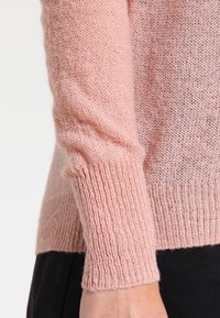 Jasnoróżowy sweter z dzianiny o miękkiej teksturze, z prążkowanymi mankietami i połączeniem delikatnej włóczki, podkreślający luźny fason.