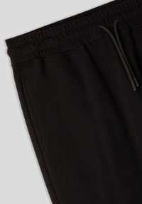 Pantaloni sportivi neri con una texture liscia, vita elastica e cordoncino. Include tasche laterali e un design a vestibilità rilassata.