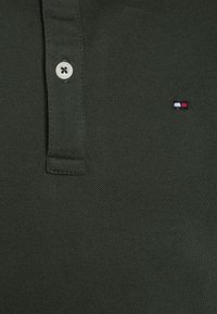 Polo shirt verde scuro realizzato in un tessuto testurizzato, con una pattina a tre bottoni e un piccolo logo ricamato in rosso, bianco e blu.