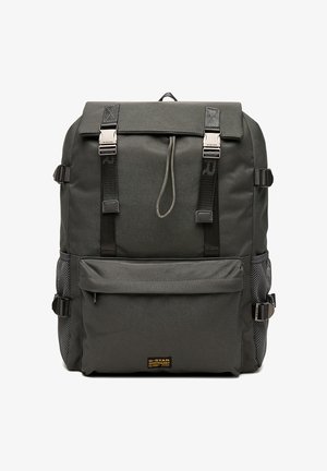 Dunkelgrauer Stoffrucksack mit Frontreißverschlusstasche, obenliegender Klappe, die mit zwei schwarzen Schnallen gesichert ist, seitlichen Netztaschen und verstellbaren Gurten.