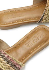 Sandales tissées avec une sangle multicolore texturée et un semelle en cuir lisse marron, comportant des détails de marque en relief et une semelle plate.