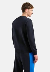 Felpa nera con collo rotondo, maniche lunghe e polsini a coste. Il tessuto appare liscio con un design minimalista.