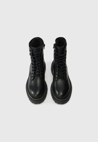 Bottines en cuir noir avec une doublure en fausse fourrure, un devant lacé et des zips sur les côtés. Bout arrondi et semelle épaisse crantée pour une bonne adhérence.