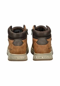 Botas de cuero marrón hasta el tobillo con un cuello de ante marrón oscuro, que presentan cremalleras a los lados y una suela de goma texturizada gris.