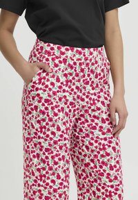 Bloemmotief wijd-uitlopende broeken met een witte basis en roze en groene bloemen, elastische tailleband en zijzakken. Gladde stof textuur.
