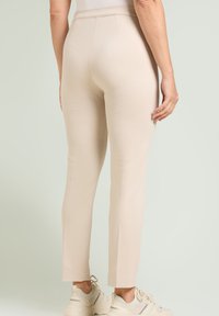 Pantalones beige ajustados con una textura suave, cintura de tiro medio y piernas entalladas. Terminados con un dobladillo limpio y combinados con zapatillas neutrales.