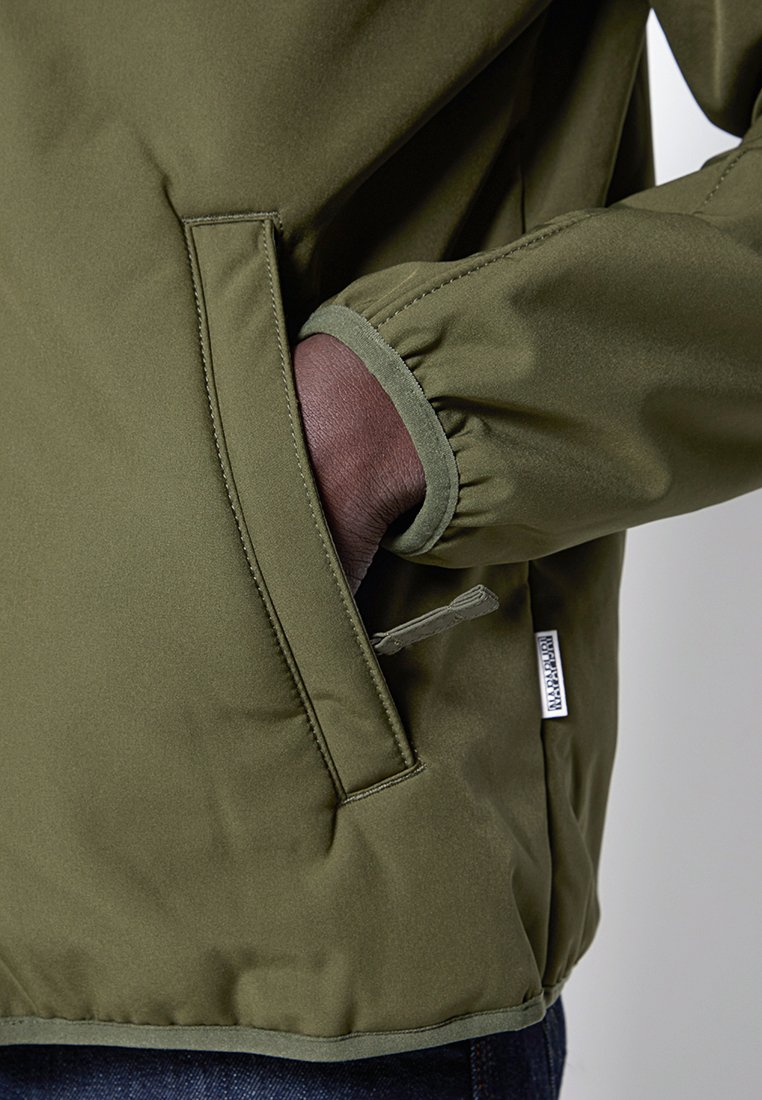 Chaqueta verde oliva con un acabado suave y mate. Presenta puños elásticos, un bolsillo lateral y una etiqueta de logo sutil. Costuras cosidas a máquina.