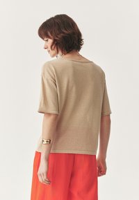 Maglione beige a maniche corte con una vestibilità rilassata, scollatura rotonda e tessuto strutturato. Abbinato a una gonna arancione; bracciale dorato in evidenza.