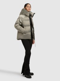 Pufferjakke i lys olivengrøn med høj krave, quiltet design og blank tekstur. Kombineret med sorte viddebukser og chunky støvler.