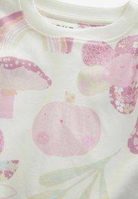 Tissu blanc avec des motifs pastel roses : citrouille souriante, champignons et motifs floraux. Texture douce avec un col rond.