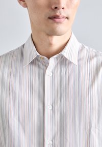 Camisa de botones a rayas con cuello, que presenta líneas delgadas en colores pastel alternos sobre un fondo blanco y dos botones en la parte frontal.
