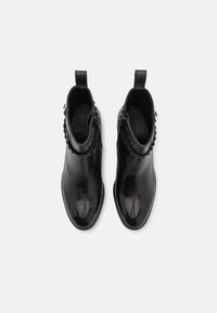 Černé kožené kotníkové boty s elegantním designem, nabízející hladkou texturu, zapínání na zip a dekorativní cvoky podél stran.