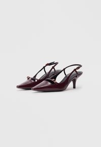 Burgundin väriä olevat nahkaiset slingback-korkokengät, joissa on terävät kärjet, leikattuja yksityiskohtia ja kultaiset varusteet. Ominaisuuksiin kuuluu matala korko ja säädettävät hihnat.