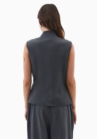 Ærmeløs, tætsiddende vest i mørkegrå struktureret stof, med høj krave og skræddersyet silhuet, samt indsnit for en kontureret pasform.