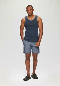 Débardeur côtelé bleu marine associé à un short bleu clair. Le mannequin se tient les mains dans les poches, portant des chaussures noires à enfiler. Tissu lisse.
