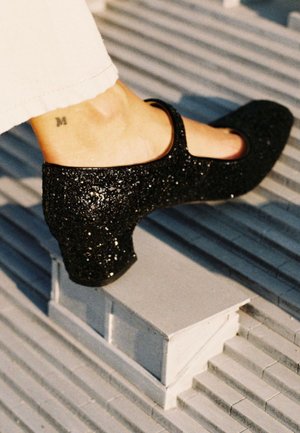 Scarpa Mary Jane nera con glitter, punta rotonda e tacco basso a blocco, dotata di cinturino alla caviglia e dettagli in pelle liscia.