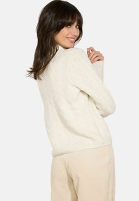 Cremfarbener, gestrickter Pullover mit strukturiertem Muster, entspannter Passform, langen Ärmeln und geripptem Saum. Kombiniert mit hellbeigen Cordhosen.
