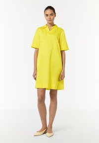 Gelbes kurzärmeliges Hemdkleid aus leichtem Stoff, knielang mit geradem Schnitt, kombiniert mit beigen spitzen Ballerinas.