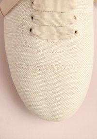 Baskets en toile beige avec un tissu texturé, des coutures visibles et des lacets plats. Bout arrondi avec un design minimal et sans accents supplémentaires.
