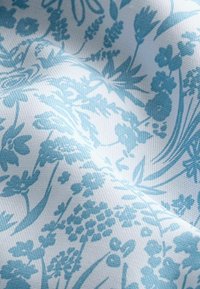 Tela floral de color azul claro que presenta varios patrones de flores y hojas sobre un fondo blanco, con una superficie texturizada y un detalle sutil.