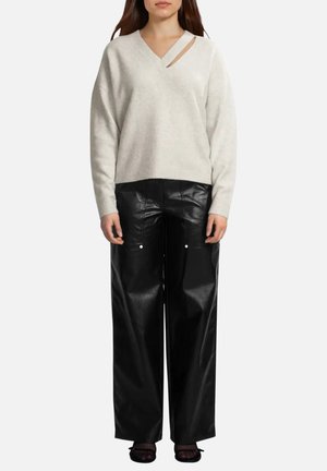 Mujer con suéter asimétrico de cuello en V color crema combinado con pantalones anchos de cuero sintético negro y zapatos negros.