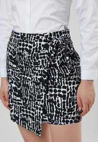Zwart-wit gestreepte wikkelrok met een asymmetrische zoom en strikdetail bij de taille, gemaakt van een lichtgewicht stof.