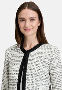 Biała żakiet z tweedu z czarnym wykończeniem przy kołnierzu i na środku, z fakturowanym wzorem i zapięciem na haczyk.