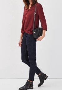 Bourgognebluse med v-hals, kombineret med mørkeblå skinny jeans. Sort skuldertaske med strukturerede detaljer og ankelstøvler med guldlynlåse.