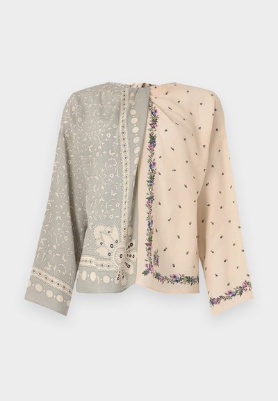 Zweifarbige Jacke: eine Seite in Grau mit floralen Stickereien und Perlenakzenten, die andere in Creme mit kleinen Blumenmustern und einer Bordüre.